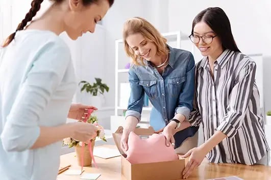 3 smiling business women prepare a package in a box from a Bullhorn integration