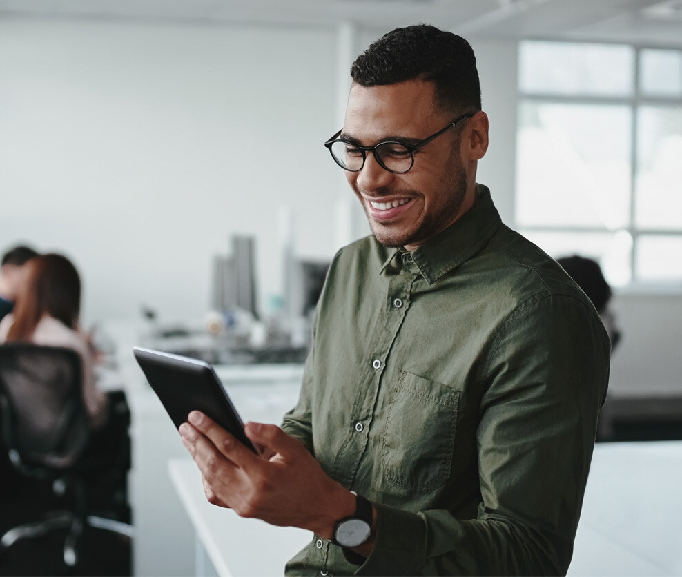 Smiling man looks a small tablet with his coworkers in the background