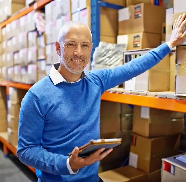 Happy business man in warehouse surrounded by boxes to ship