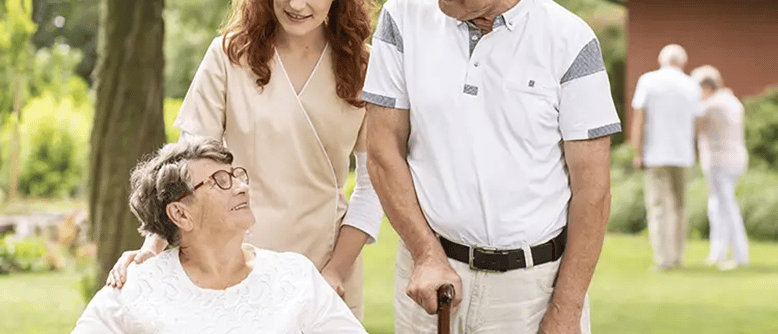 Un employé d'un établissement de vie communautaire aide une dame âgée en fauteuil roulant et son mari, qui utilise une canne.