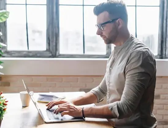 Businessman wearing glasses in an office works on a laptop