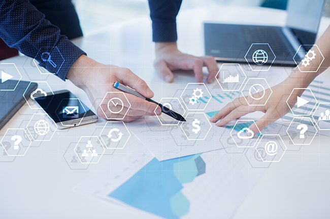 Hands gesture at papers on a conference table with stylized graphics for time, money, graphs, cloud computing, and others
