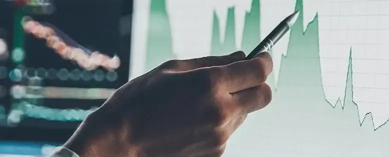 Businessman uses a pen to point at a computer screen displaying a wave graph with other charts in the background