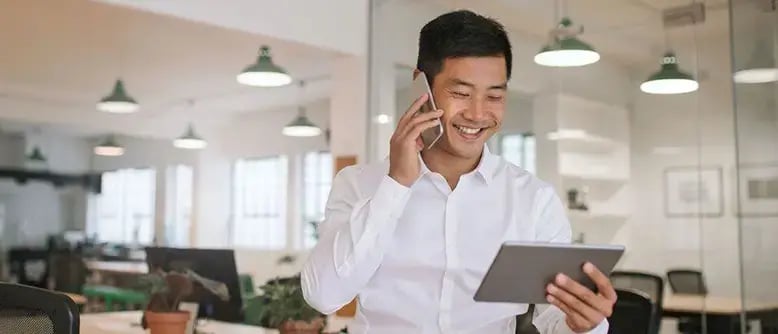 Smiling businessperson at an office table, reviewing Sage Intacct integrations on a tablet while speaking on a smartphone