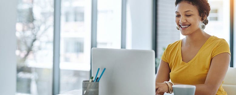 Smiling businesswoman uses a laptop on a desk in a window office