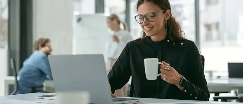 Lady looking at computer screen about SAP cloud ERP software management with a coffee smiling.