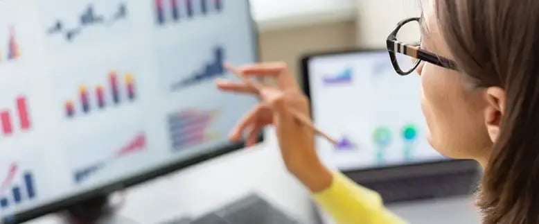 Woman wearing glasses examines graphs on a computer screen