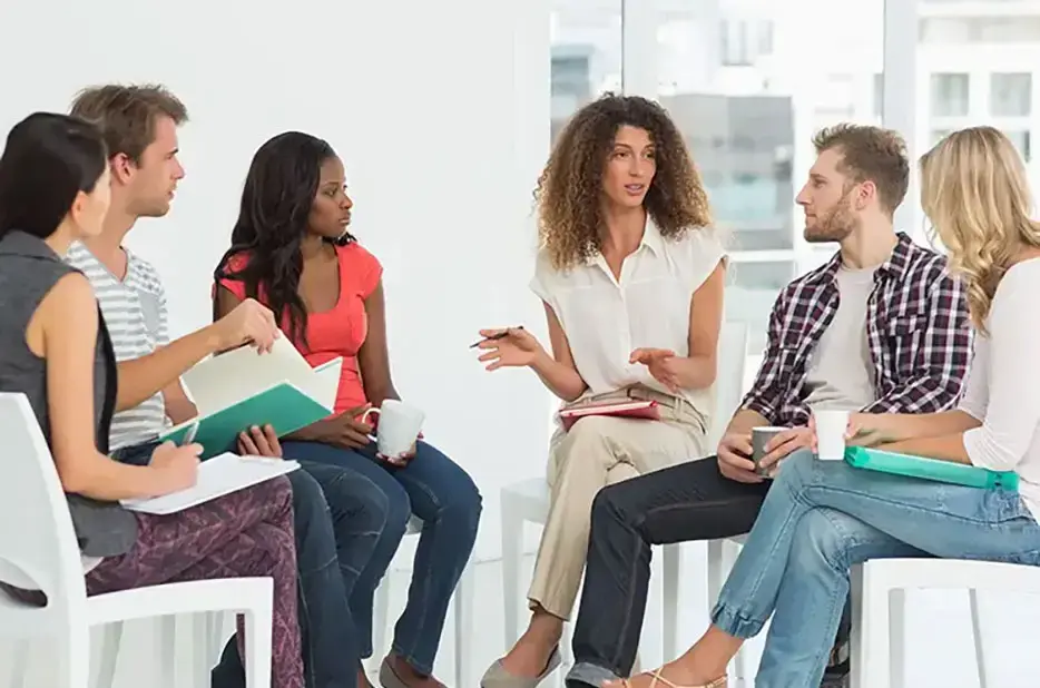 Six employés d'un service d'aide à la vie en communauté, assis sur des chaises dans un bureau spacieux, discutent de finances.